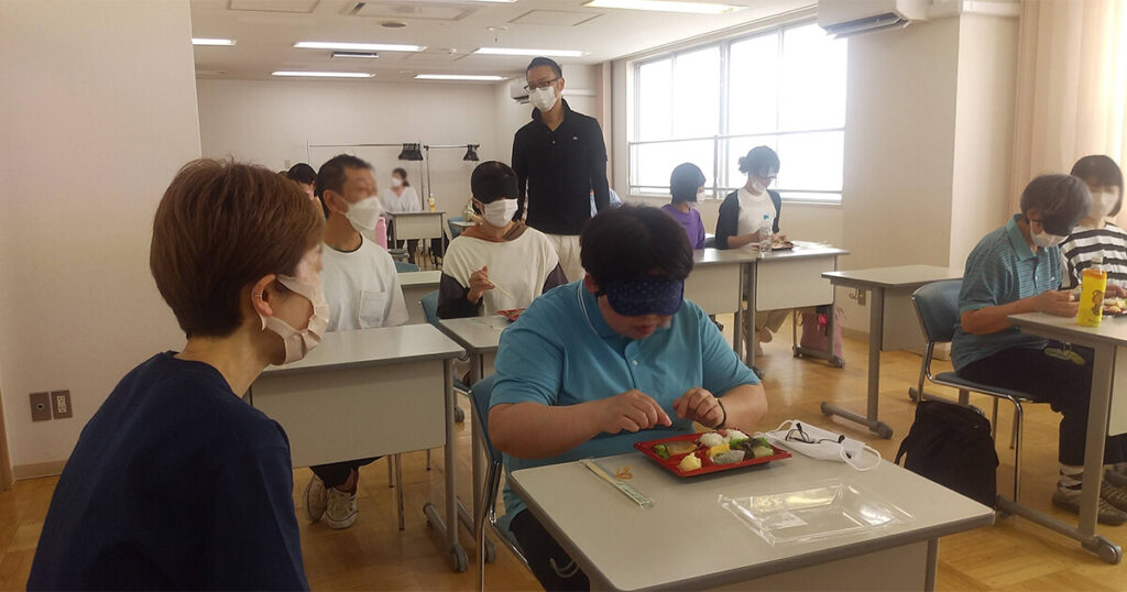 アイマスクを体験しながらお弁当を食べる受講生